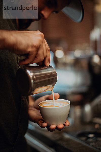 Barista gießt im Café Milch in eine Tasse Milchkaffee  Nahaufnahme der Hände
