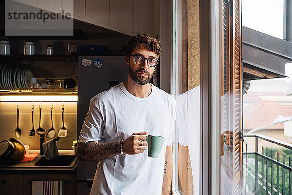 Mittlerer erwachsener Mann mit Kaffee am Wohnungsfenster  Porträt