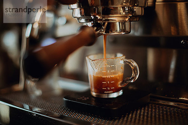 Barista gießt frischen Kaffee in Messbecher auf Kaffeemaschine im Café  flacher Fokus