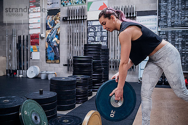 Junge Frau hebt Hantelscheibe im Fitnessstudio