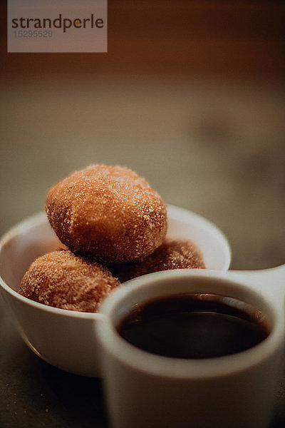 Eine Tasse schwarzer Kaffee und eine Schüssel Donuts auf einem Kaffeetisch  Nahaufnahme mit seichtem Fokus