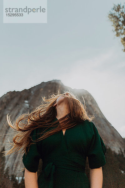 Junge Frau mit fliegendem Haar  die vor dem sonnenbeschienenen Berg nach oben schaut  Yosemite Village  Kalifornien  USA