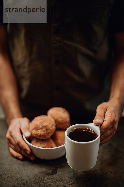 Barista platziert schwarzen Kaffee und Doughnuts auf Café-Theke  abgeschnittener flacher Fokus