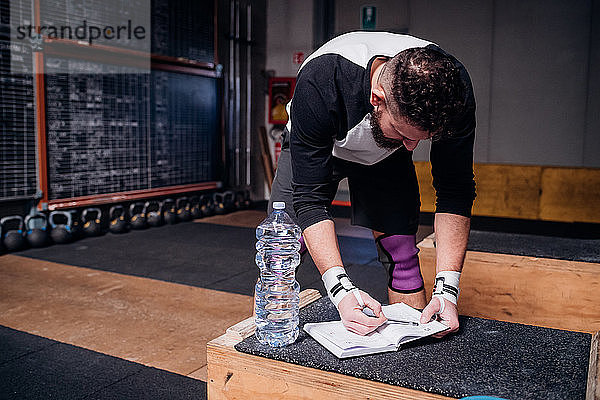 Junger Mann liest Checkliste am Notebook im Fitnessstudio