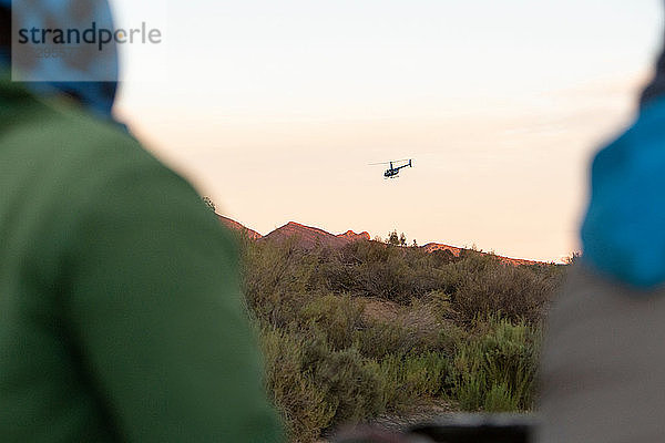 Zwei Personen beobachten Hubschrauber über der Berglandschaft  über die Schulter gesehen  Kapstadt  Westkap  Südafrika