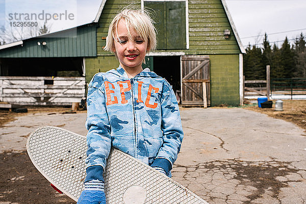 Blonder Junge mit Skateboard auf dem Bauernhof  Porträt
