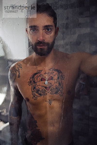 Mittelgroßer erwachsener Mann mit tätowierter Brust in der Dusche  Porträt