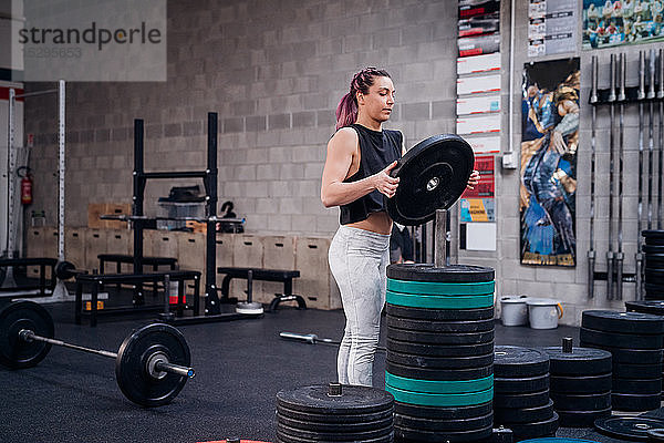 Junge Frau legt Hantelscheibe im Fitnessstudio auf das Regal