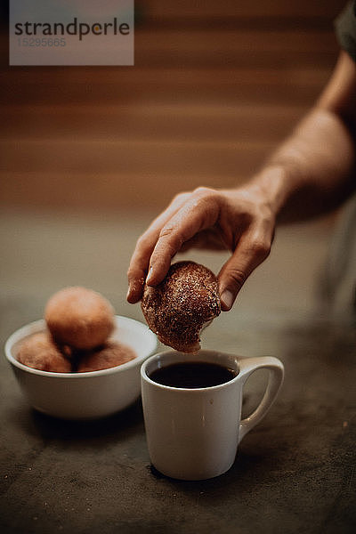 Mann taucht Doughnut in schwarzen Kaffee an Café-Tisch  abgeschnittener flacher Fokus