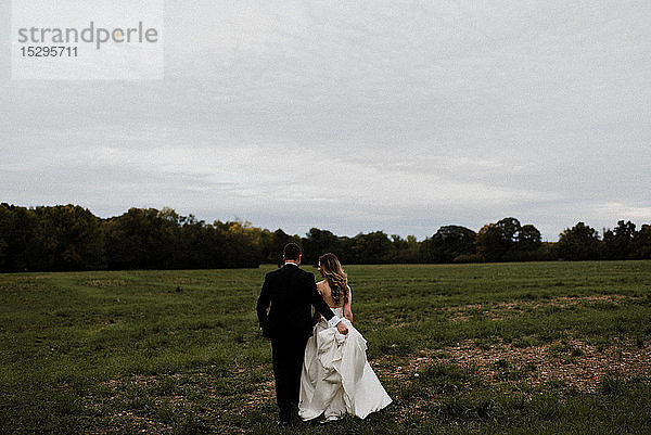 Romantischer junger Bräutigam mit Brautkleidschleppe im Feld  Rückansicht