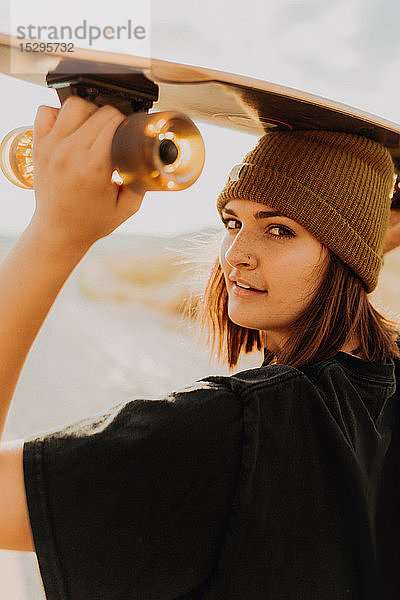 Junge Frau mit Skateboard auf dem Kopf auf einer Landstrasse  Portrait  Exeter  Kalifornien  USA