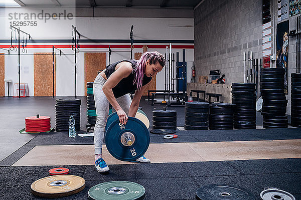 Junge Frau legt im Fitnessstudio Hantelscheibe in die Hantel