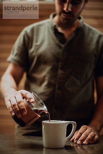 Barista gießt frischen schwarzen Kaffee in Tasse auf Café-Theke  seichter Fokus