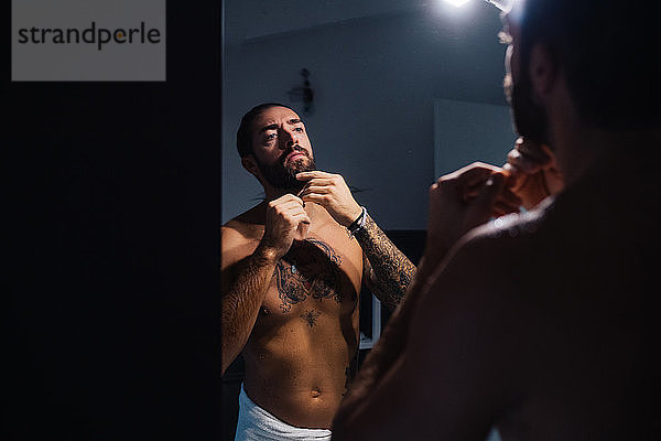 Mittelgroßer erwachsener Mann mit Tattoos  die den Bart am Badezimmerspiegel beschneiden