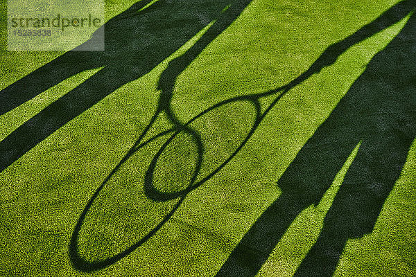 Angeschnittene Schatten von zwei Tennisspielern mit Tennisschlägern auf grünem Rasen