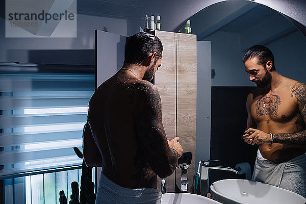 Mittelgroßer Mann mit Tätowierungen macht sich am Badezimmerspiegel bereit