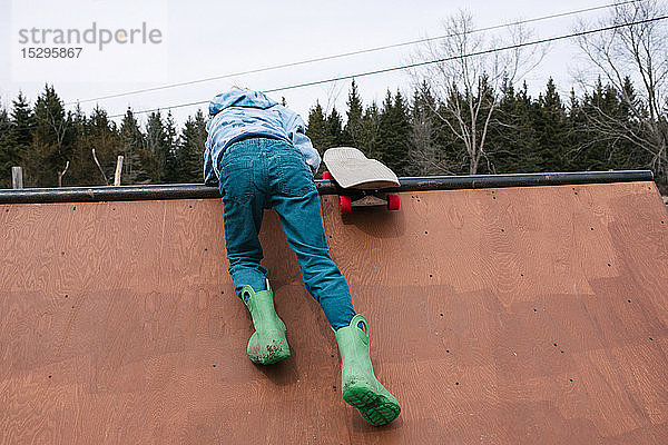 Junge klettert auf die Spitze der Skateboard-Rampe  Rückansicht