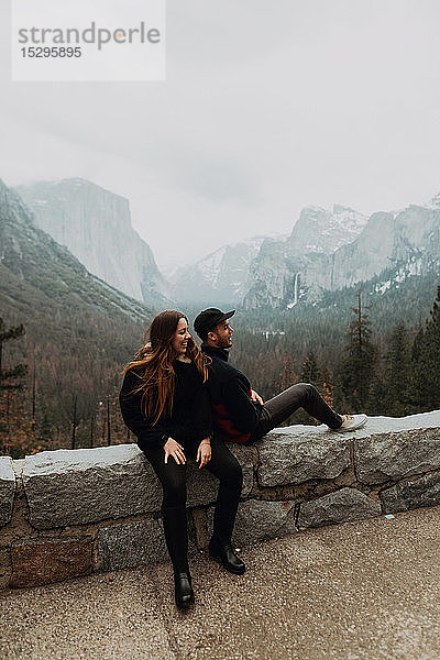 Junges Paar sitzt auf einer Mauer in einer Berglandschaft  Yosemite Village  Kalifornien  USA