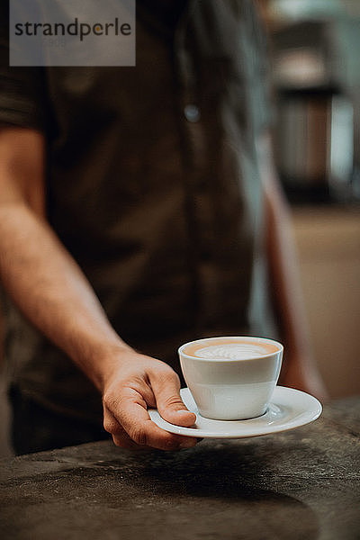 Barista stellt Tasse Milchkaffee auf Café-Theke  abgeschnittener flacher Fokus