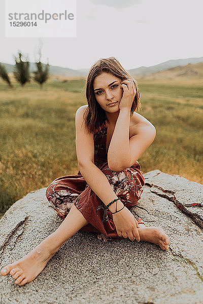 Schöne junge Frau sitzt im Schneidersitz auf einem Felsblock  Portrait  Exeter  Kalifornien  USA