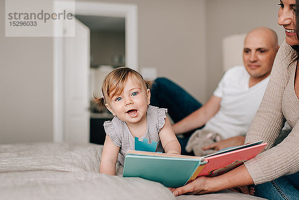 Mutter und Vater im Bett mit Baby-Tochter mit Geschichtenbuch  Porträt