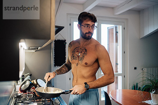 Mittelgroßer Mann mit Tätowierungen beim Frühstücken in der Bratpfanne