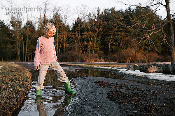 Junge tritt mit dem Knöchel tief in eine ländliche Schmelzwasserpfütze