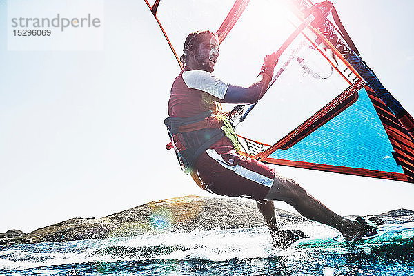 Junger Mann lehnt sich beim Windsurfen auf sonnenbeschienenen Meereswellen zurück  Limnos  Khios  Griechenland