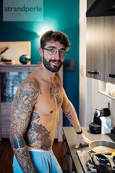 Mittelgroßer erwachsener Mann mit tätowierter Brust bei der Frühstücksvorbereitung  Porträt