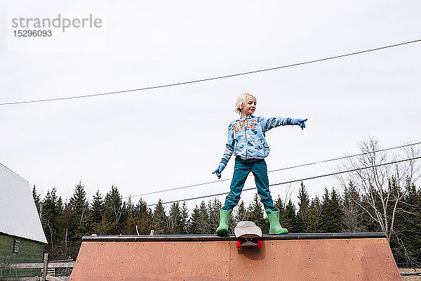 Junge steht oben auf der Skateboard-Rampe und zeigt
