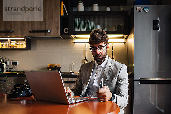 Mittelgroßer erwachsener Mann am Küchentisch sitzend mit Laptop und Kreditkarte