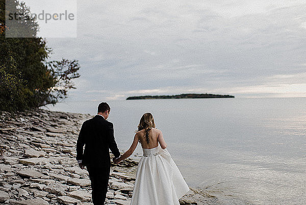 Romantische junge Braut und Bräutigam schlendern am Hochzeitstag am Seeufer entlang
