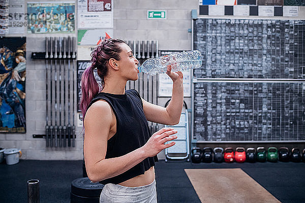 Junge Frau trinkt Wasser im Fitnessstudio