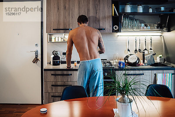 Mittelgroßer erwachsener Mann  der das Frühstück am Küchenherd zubereitet  Rückansicht