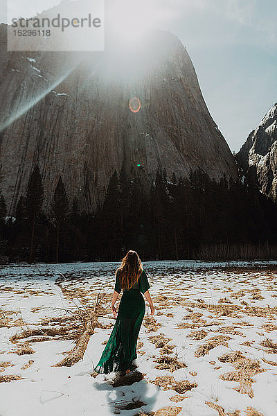 Junge Frau in langem Kleid  stehend in sonniger  schneebedeckter Berglandschaft  Rückansicht  Yosemite Village  Kalifornien  USA