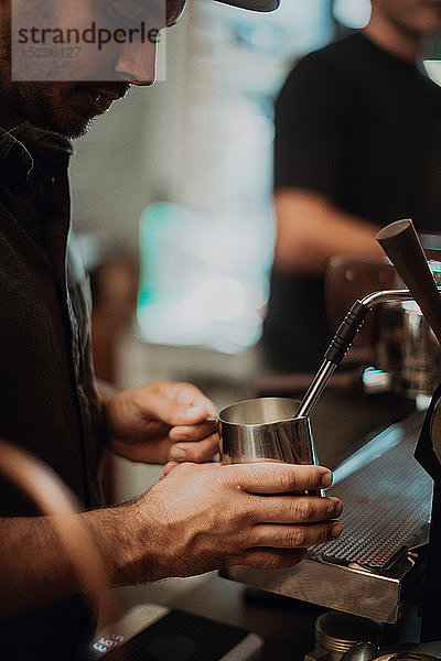 Barista erhitzt Milchkännchen auf Kaffeemaschine im Café  abgeschnittener flacher Fokus