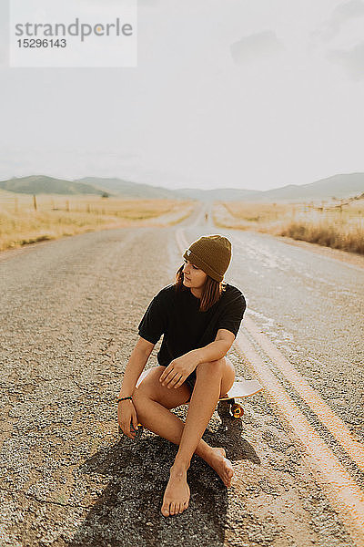 Junge Skateboardfahrerin sitzt auf einer Landstraße  Exeter  Kalifornien  USA