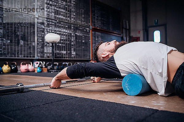 Junger Mann massiert im Fitnessstudio den unteren Rücken mit einer Schaumstoffrolle