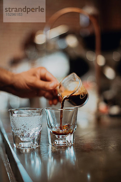 Barista gießt frischen Kaffee in ein Trinkglas an der Kaffeetheke  Detail der Hand