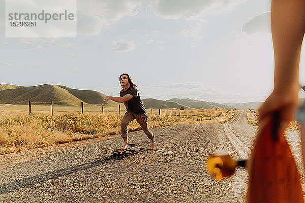 Junger barfüssiger männlicher Skateboarder beim Skateboarden auf ländlicher Strasse  Freundin schaut zu  Exeter  Kalifornien  USA