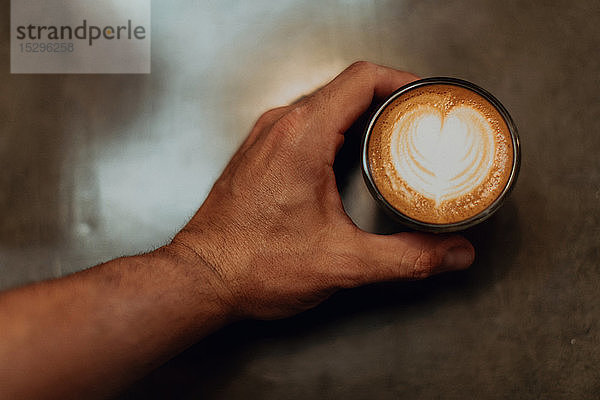 Barista stellt Tasse Milchkaffee mit Herzform auf die Café-Theke  über Kopf in Nahaufnahme