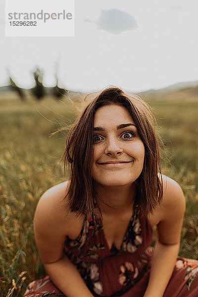 Junge Frau sitzt im Feld aus langem Gras und zieht ein Gesicht  Portrait  Exeter  Kalifornien  USA