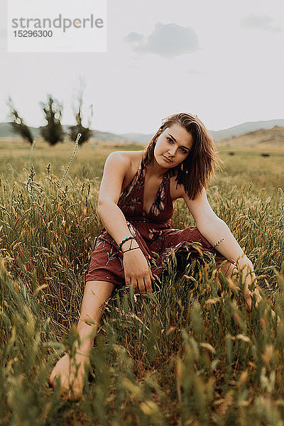Schöne junge Frau sitzt auf einem Feld aus langem Gras  Portrait  Exeter  Kalifornien  USA