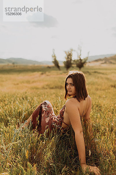 Hübsche junge Frau sitzt auf einem Feld aus langem Gras und schaut über ihre Schulter  Porträt  Exeter  Kalifornien  USA