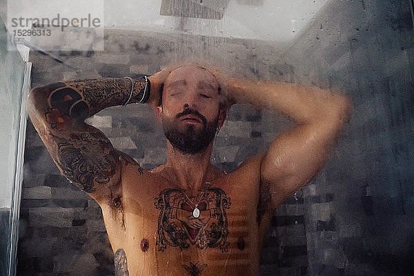 Mittelgroßer erwachsener Mann mit tätowierter Brust in der Dusche