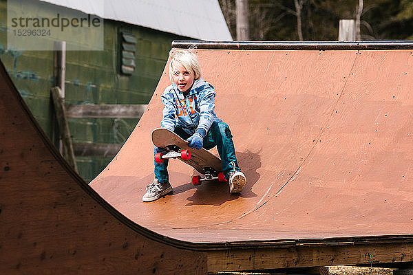 Junge bereitet sich darauf vor  sich auf einer hölzernen Skateboard-Rampe auf ein Skateboard zu setzen