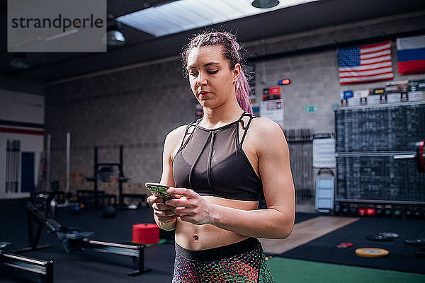 Junge Frau beim Training  Blick auf Smartphone im Fitnessstudio