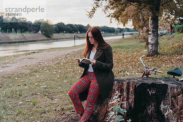 Junge Frau mit langen roten Haaren liest Buch am Flussufer  Florenz  Toskana  Italien
