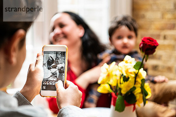 Junge macht Smartphone-Foto Mutter und Kleinkind Bruder feiern Muttertag  Blick über die Schulter