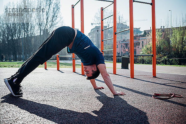 Gymnastik im Fitnessstudio im Freien  junger Mann in abwärtsgerichteter Hunde-Yoga-Pose